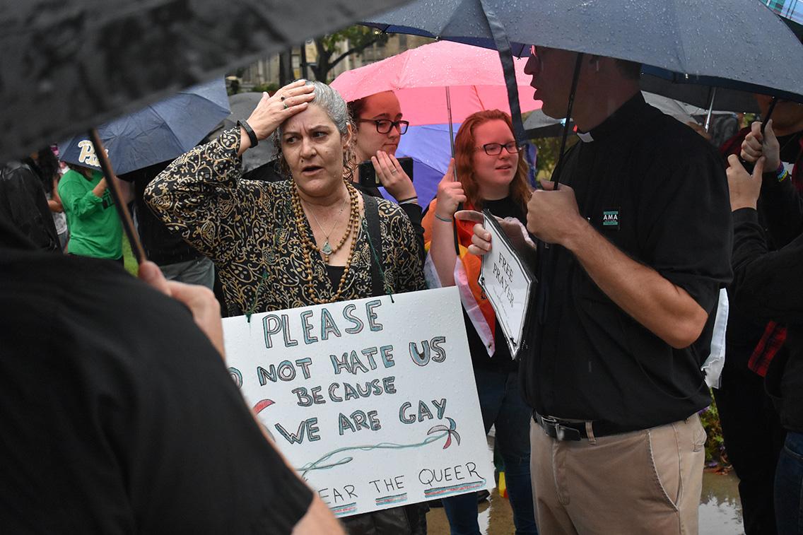 An activist stands next to a man offering prayers outside the Cathedral of Learning