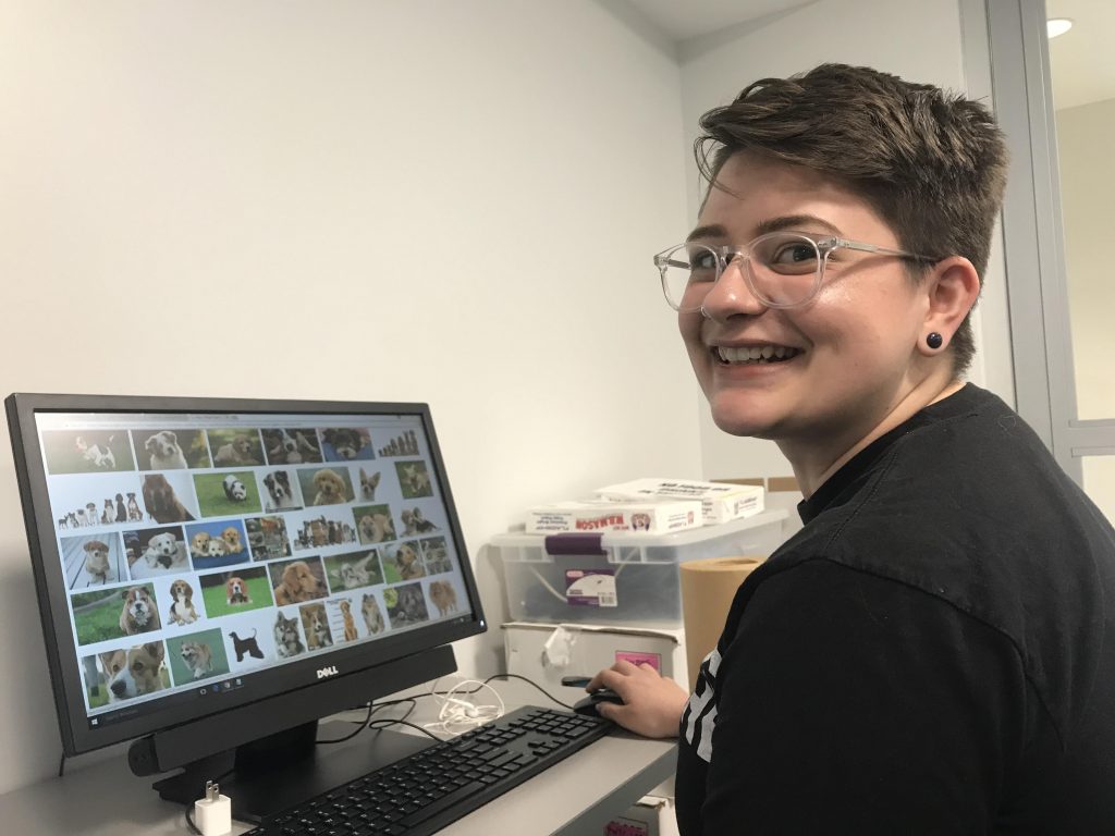 alternative studying Student in front of computer screen covered with pictures of puppies turns to smile at camera