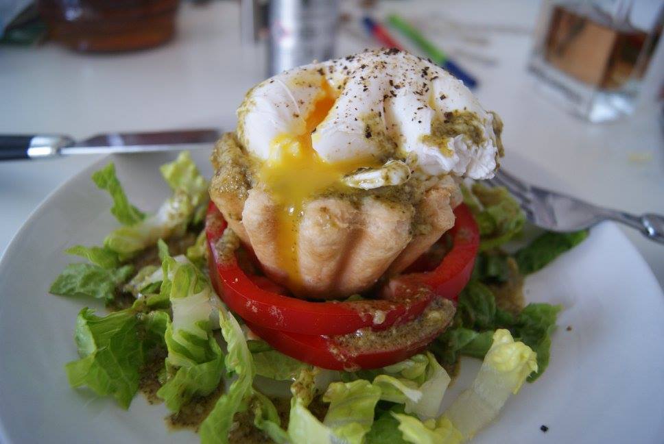 Poached egg on mashed potato filled pastry cup resting on a bed of salad with honey and mustard dressing and black pepper.