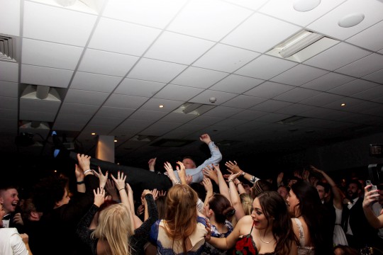 Nick Petford crowd-surfing. A university vice chancellor has been accused of bringing his profession into disrepute after he was pictured necking shots and CROWD-SURFING at a boozy student awards bash. See NTI story NTIUNI. Professor Nick Petford, who earns over £200,000 a year in his role at the University of Northampton, was seen drinking heavily and having a DANCE OFF with students. He has since been dubbed the "Wolf of Northampton" - a reference to Martin Scorcese's film 'The Wolf of Wall Street" following his boozy antics. The 53-year-old had been attending the Student's Sports Awards held at a function room at Northampton Saints Rugby Club on March 20. Professor Petford was among a number of senior staff who handed out awards in a number of different categories. After a three course meal comedian Lee Nelson entertained the crowd of 400 where he encouraged Mr Petford and Jane Bunce, the university's Director of Student and Academic Services, to neck glasses of wine. They then had a dance competition before being pictured crowd-surfing across a sea of students who passed them over their heads.