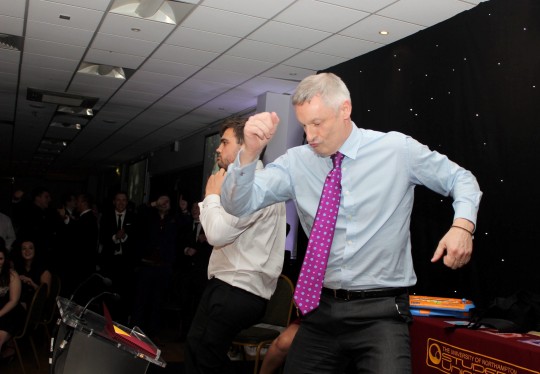 Nick Petford having a dance off. A university vice chancellor has been accused of bringing his profession into disrepute after he was pictured necking shots and CROWD-SURFING at a boozy student awards bash. See NTI story NTIUNI. Professor Nick Petford, who earns over £200,000 a year in his role at the University of Northampton, was seen drinking heavily and having a DANCE OFF with students. He has since been dubbed the "Wolf of Northampton" - a reference to Martin Scorcese's film 'The Wolf of Wall Street" following his boozy antics. The 53-year-old had been attending the Student's Sports Awards held at a function room at Northampton Saints Rugby Club on March 20. Professor Petford was among a number of senior staff who handed out awards in a number of different categories. After a three course meal comedian Lee Nelson entertained the crowd of 400 where he encouraged Mr Petford and Jane Bunce, the university's Director of Student and Academic Services, to neck glasses of wine. They then had a dance competition before being pictured crowd-surfing across a sea of students who passed them over their heads.