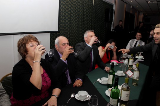 Nick Petford and other university staff being encouraged to drink by comedian Lee Nelson. A university vice chancellor has been accused of bringing his profession into disrepute after he was pictured necking shots and CROWD-SURFING at a boozy student awards bash. See NTI story NTIUNI. Professor Nick Petford, who earns over £200,000 a year in his role at the University of Northampton, was seen drinking heavily and having a DANCE OFF with students. He has since been dubbed the "Wolf of Northampton" - a reference to Martin Scorcese's film 'The Wolf of Wall Street" following his boozy antics. The 53-year-old had been attending the Student's Sports Awards held at a function room at Northampton Saints Rugby Club on March 20. Professor Petford was among a number of senior staff who handed out awards in a number of different categories. After a three course meal comedian Lee Nelson entertained the crowd of 400 where he encouraged Mr Petford and Jane Bunce, the university's Director of Student and Academic Services, to neck glasses of wine. They then had a dance competition before being pictured crowd-surfing across a sea of students who passed them over their heads.